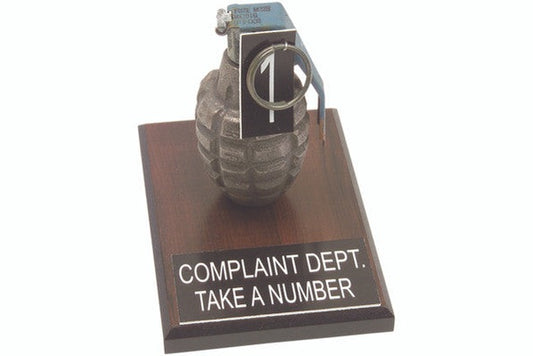 desk display of a granade on a wood stand with writing complaint department take a number